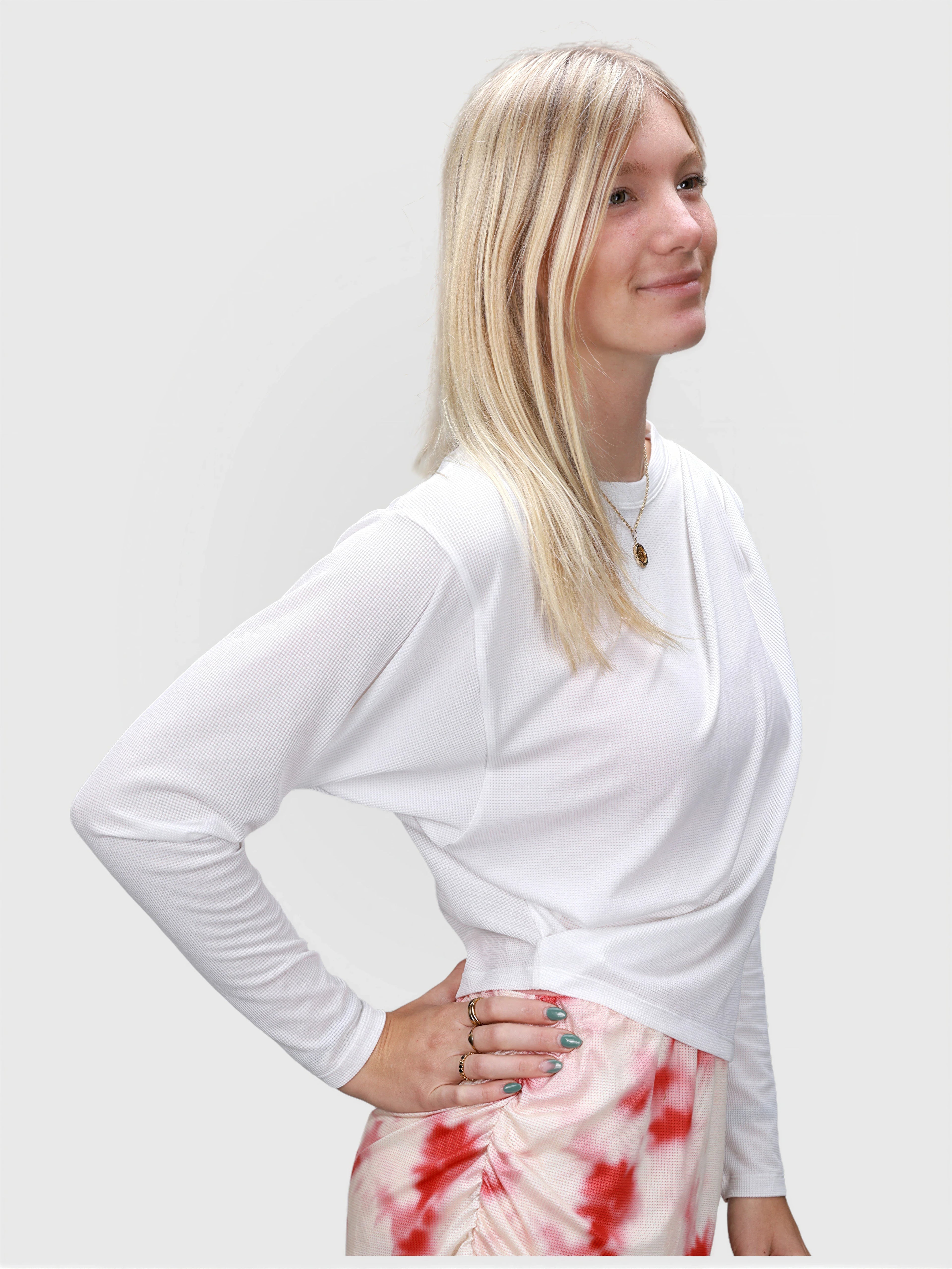 Woman modeling white Airy Twist Long Sleeve by MUEV paired with red and white patterned skirt for pickleball clothing
