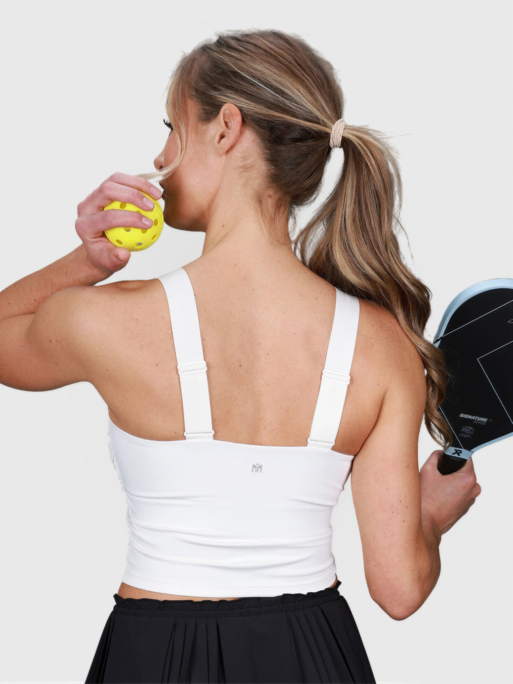 Back view of woman wearing white Airy Twist Tank by MUEV holding a padel paddle and yellow ball for padel apparel