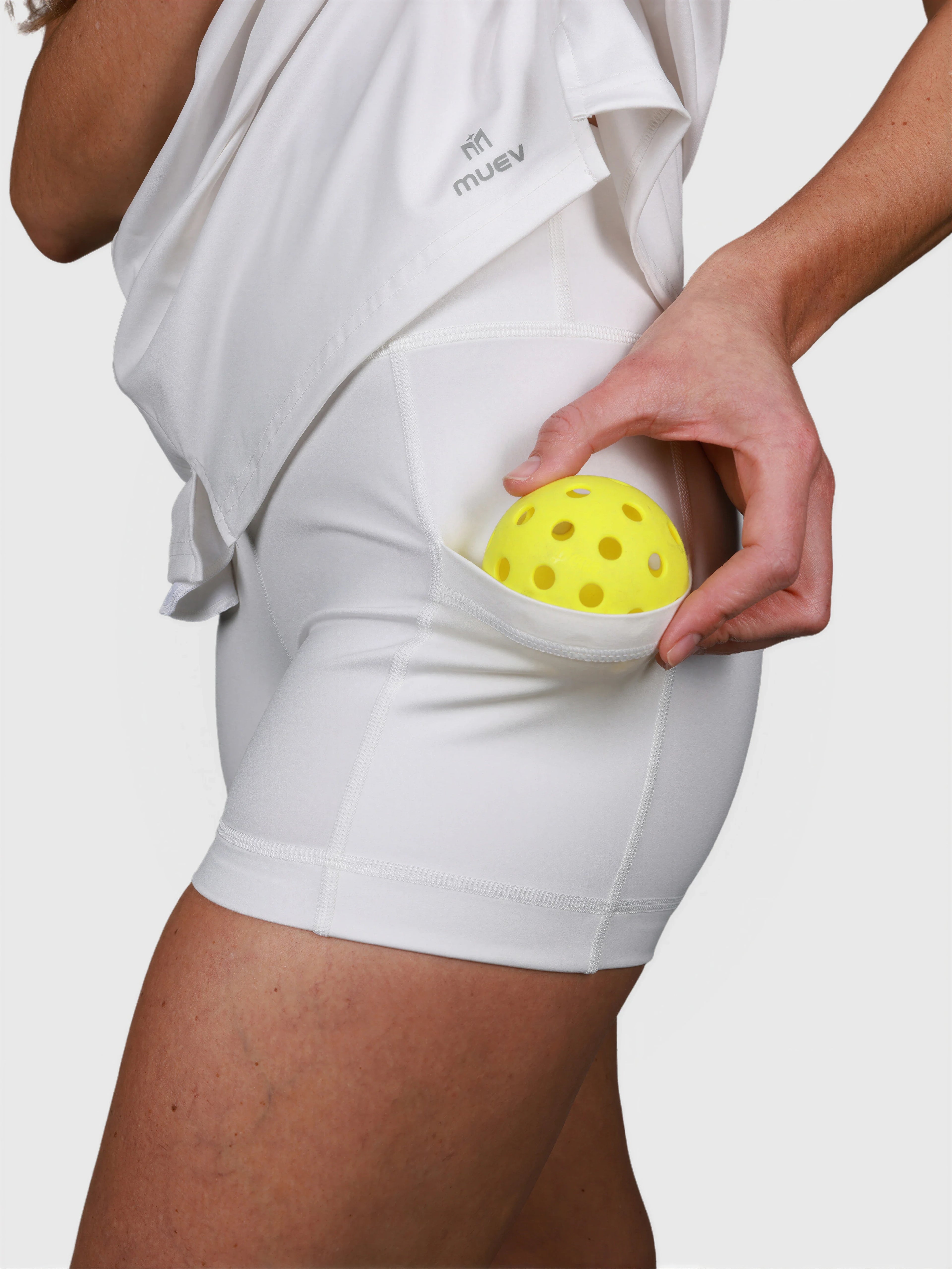 Close-up of white Open Back Polo Dress by MUEV showing integrated shorts with pocket holding yellow pickleball ball