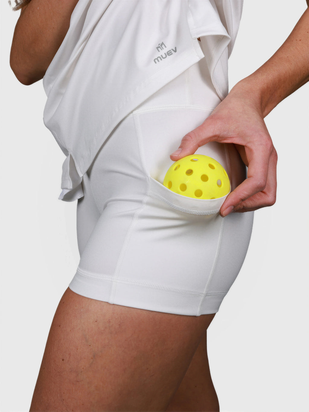 Close-up of white Power Performance Dress by MUEV showing built-in pocket holding yellow pickleball ball for padel apparel